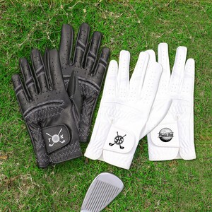 May include: Black and white golf gloves with stitched details and logos, alongside a golf club on green grass. The gloves have small perforations for breathability. One pair is black, the other white.