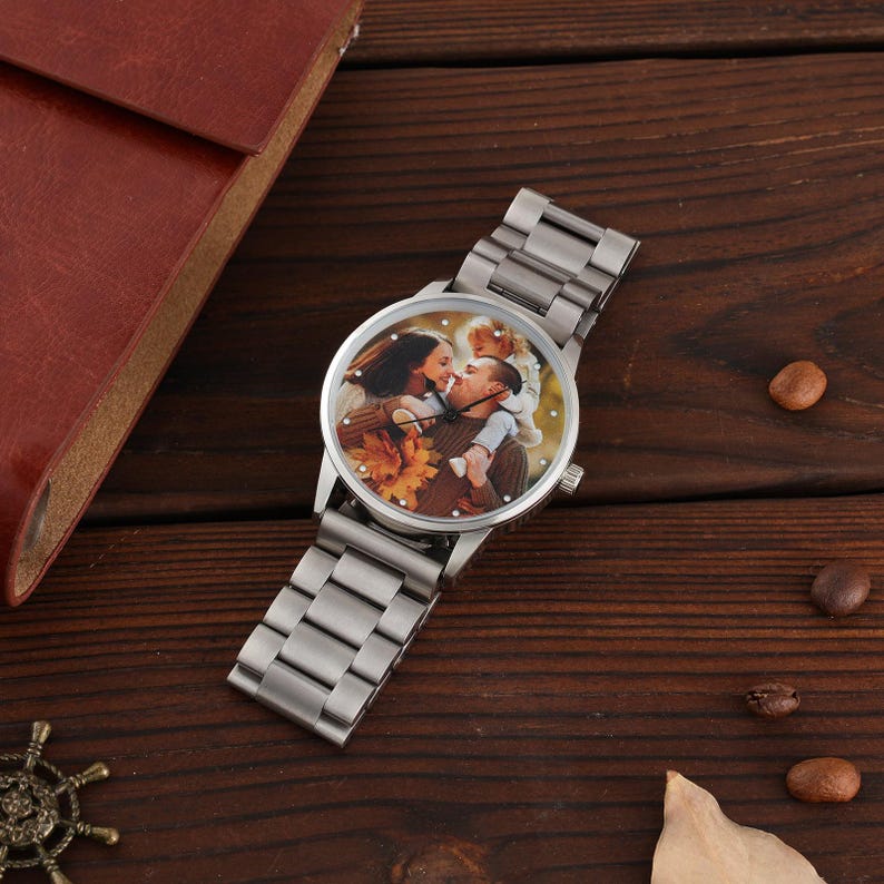 May include: A silver wristwatch with a custom photo on the watch face. The watch has a stainless steel strap and a round face showing a family portrait. It is set against a dark wooden surface.