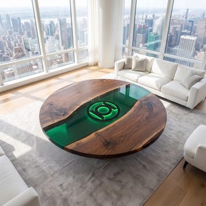 Op de afbeelding: Een ronde salontafel met een natuurlijke houten plaat met een boomkant en een centrale inleg van doorschijnende groene hars. Het harsgedeelte bevat een oplichtend groen, cirkelvormig Green Lantern logo in het midden van de tafel.