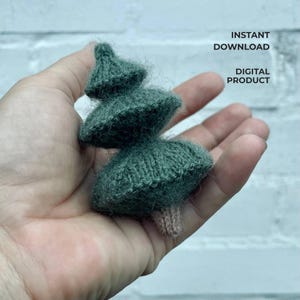 May include: A small, handmade, knitted Christmas tree in shades of green. The tree has three tiers and a small, light brown trunk. The words "INSTANT DOWNLOAD" and "DIGITAL PRODUCT" are printed on the image.