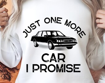 May include: White sweatshirt with the text "JUST ONE MORE CAR I PROMISE" in black. A black car graphic is centered on the front. The sweatshirt is worn by a person.