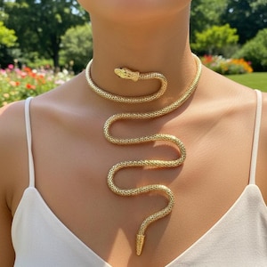 May include: Gold-toned snake necklace. The necklace wraps around the neck and drapes down the chest, with a snake head at the neck and a tail at the bottom. The jewelry has a textured, scale-like pattern.