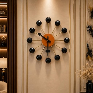 Könnte beinhalten: Eine moderne Wanduhr mit einzigartigem Design. Die Uhr hat eine orangefarbene Mitte, goldfarbene Speichen und schwarze kugelförmige Akzente. Die Zeiger sind schwarz, und die Gesamtästhetik ist modern und stilvoll.