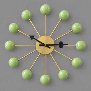 Può includere: Un orologio da parete con un quadrante centrale circolare color ottone e dodici sottili raggi metallici color oro che si irradiano verso l'esterno. Ogni raggio termina con una sfera liscia verde chiaro. Le lancette sono nere.