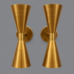 May include: A pair of wall-mounted light fittings featuring a brushed brass finish. Each fitting consists of two symmetrical, cone-shaped shades joined at a central cylindrical connector, attached to a circular wall plate for mounting purposes.