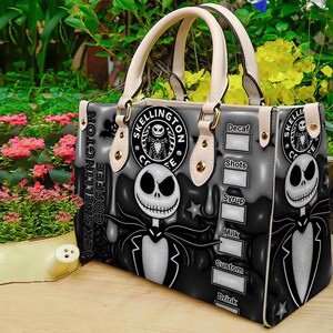 Op de afbeelding: Een zwart-witte handtas met Jack Skellington uit The Nightmare Before Christmas. De tas heeft cr&egrave;mekleurige handvatten en accenten, met de woorden "Jack Skellington Coffee" en een koffiebestelmenu aan de zijkant.