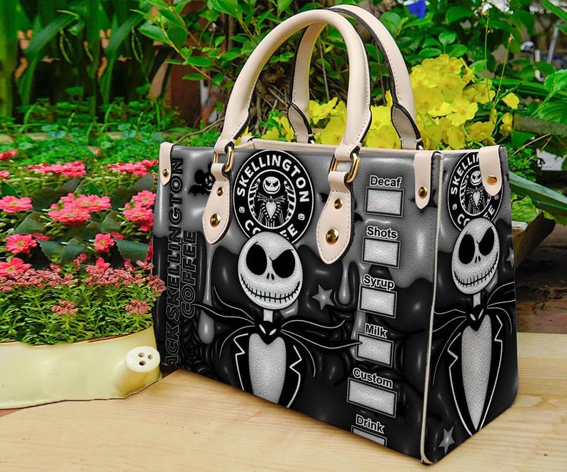 Op de afbeelding: Een zwart-witte handtas met Jack Skellington uit The Nightmare Before Christmas. De tas heeft cr&egrave;mekleurige handvatten en accenten, met de woorden "Jack Skellington Coffee" en een koffiebestelmenu aan de zijkant.
