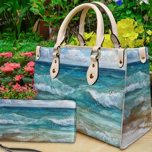 May include: A handbag and matching wallet set featuring a watercolor ocean wave design in shades of blue, teal, and white. The handbag has cream-colored handles and accents. The wallet has a wrist strap.