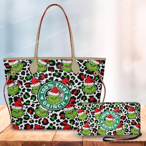 May include: A tote bag and matching wallet featuring a Grinch design. The bags have a white and black leopard print background with green Grinch faces wearing Santa hats. The tote bag has tan handles and red trim. The wallet has a black wrist strap.