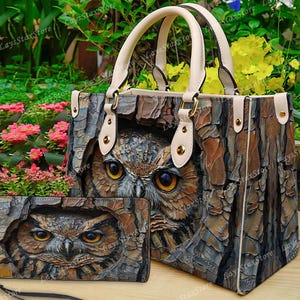 May include: A handbag and wallet set featuring an owl design. The bag has cream-colored handles and a textured, bark-like pattern with an owl's face. The wallet mirrors the bag's design, creating a cohesive accessory set.