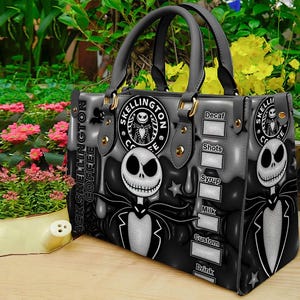 Op de afbeelding: Een zwarte en grijze handtas met een ontwerp ge&iuml;nspireerd op Jack Skellington. De tas heeft twee handvatten en goudkleurige hardware. Het ontwerp bevat de tekst "Jack Skellington Coffee" en een afbeelding van Jack Skellington.