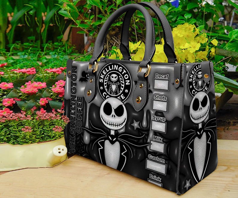Op de afbeelding: Een zwarte en grijze handtas met een ontwerp ge&iuml;nspireerd op Jack Skellington. De tas heeft twee handvatten en goudkleurige hardware. Het ontwerp bevat de tekst "Jack Skellington Coffee" en een afbeelding van Jack Skellington.