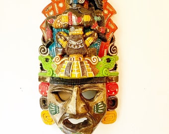 May include: A colorful, hand-painted wooden mask depicting a Mayan deity. The mask features intricate details, including a feathered headdress, a large, expressive face, and geometric patterns.