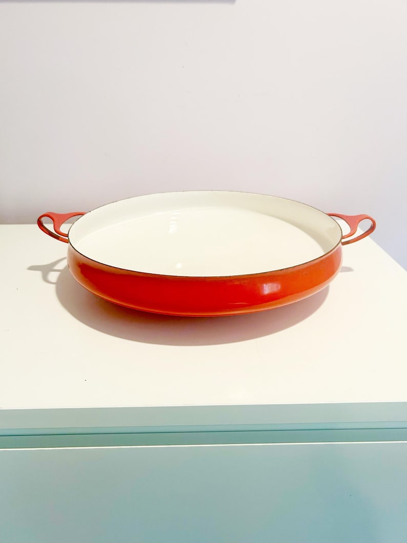 May include: A red enamel cast iron baking dish with two handles. The dish has a white interior.