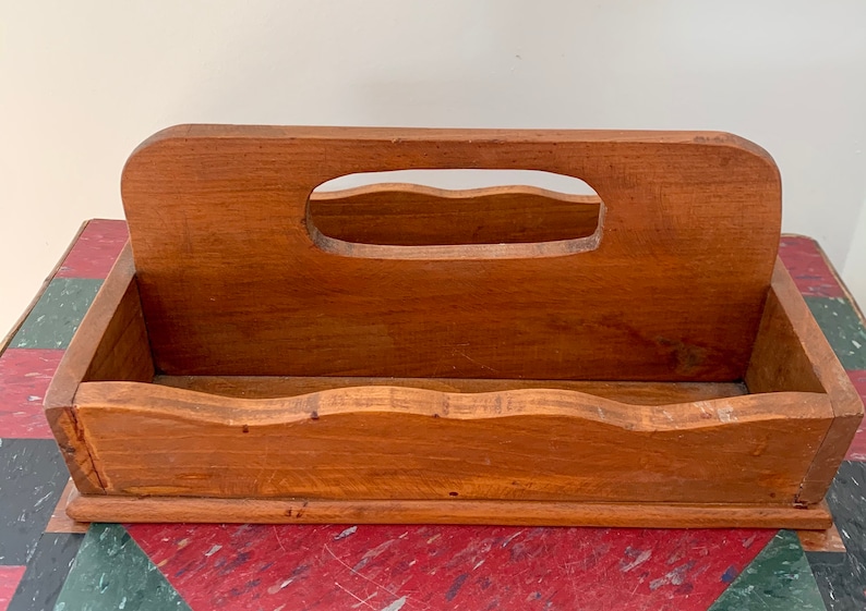 May include: A wooden box with a handle on the top. The box has a wavy edge and is made of light brown wood.