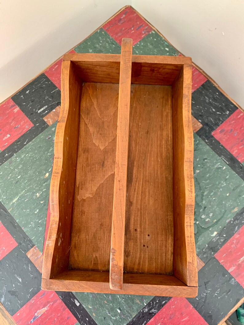 May include: A wooden tool caddy with a divided interior and a handle. The caddy is made of natural wood with a light brown finish.
