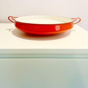 May include: Orange enamel cast iron serving dish with white interior and two handles.