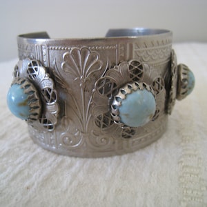 Puede incluir: Un brazalete de plata con un diseño adornado y tres piedras cabujón de color azul claro.