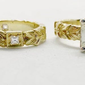May include: Two gold wedding bands with intricate floral designs. One band features a small square diamond, while the other has a larger emerald-cut diamond.
