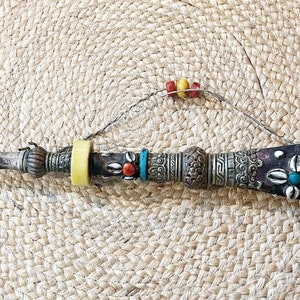 May include: A long, ornate, silver and wood pipe with a decorative mouthpiece and a brown leather body adorned with shells and colorful beads.