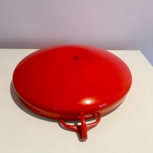 May include: A red enamel cast iron pan with two handles. The pan is upside down and the bottom is visible.