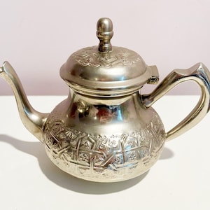 Pode incluir: Uma chaleira de prata com um design ornamentado e uma tampa. A chaleira tem um corpo redondo e um bico curvo.