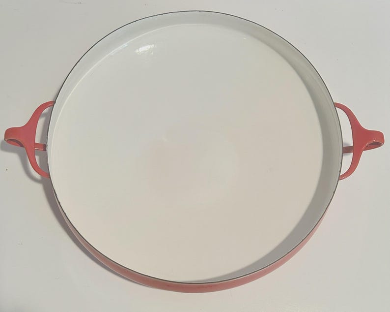 May include: Red enamel cast iron serving dish with two handles. The dish is round and has a white interior.