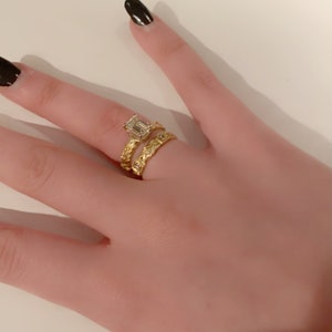 May include: A gold ring with an emerald cut diamond and a gold band with a braided design.