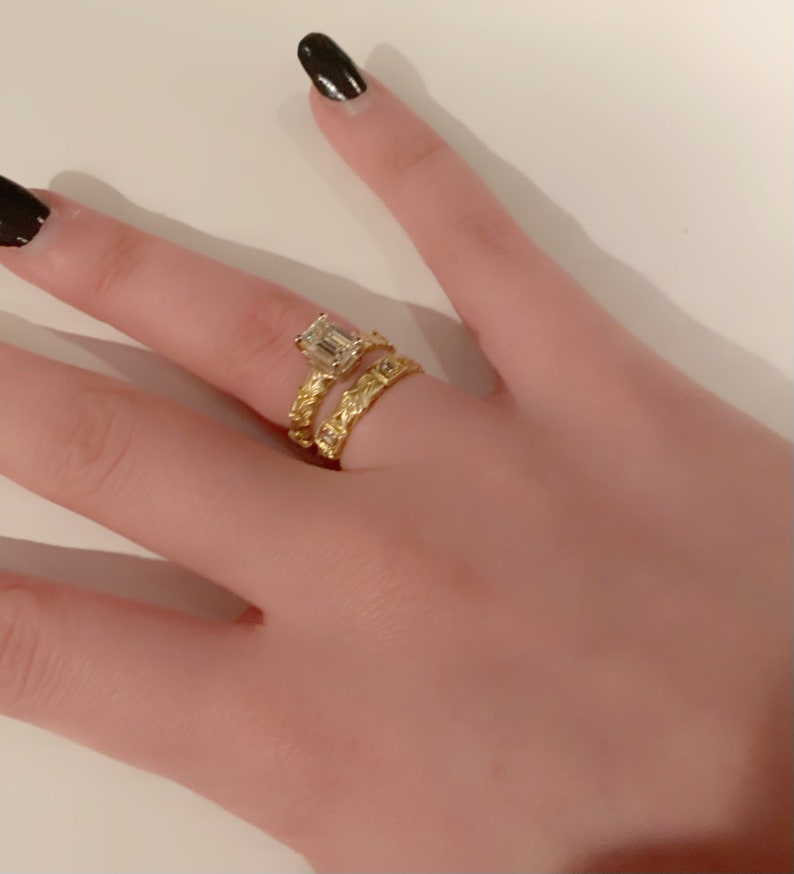 May include: A gold ring with an emerald cut diamond and a gold band with a braided design.