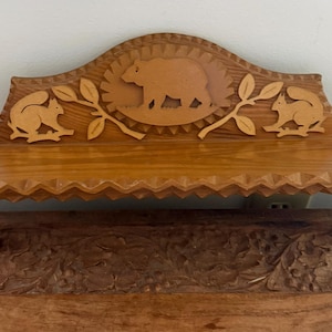 Peut inclure: Étagère en bois avec un motif sculpté représentant un ours au centre et des écureuils de chaque côté. L'étagère a un bord festonné et est soutenue par deux pieds. Le bois a une teinte chaude et naturelle.