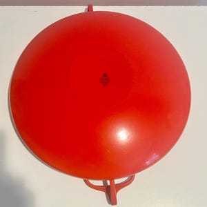 May include: A bright red, round, metal serving dish with two handles. The dish has a slightly raised center and a smooth surface.