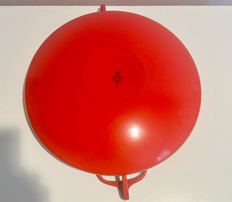 May include: A bright red, round, metal serving dish with two handles. The dish has a slightly raised center and a smooth surface.