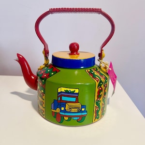May include: A green painted metal teapot with a red handle and spout. The teapot is decorated with a colorful truck design and floral patterns.