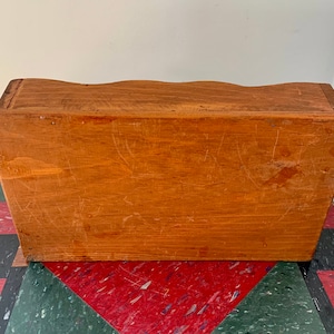 May include: A wooden box with a simple design. The box has a light brown color and a smooth surface. The box is made of wood and has a rectangular shape.