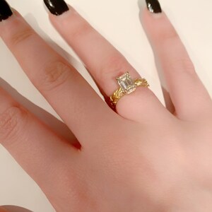 May include: A gold ring with a braided band and an emerald-cut diamond.