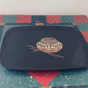 Może przedstawiać: Czarna taca do serwowania z południowo-zachodnim wzorem przedstawiającym brązową i białą ceramiczną doniczkę z czerwonymi i białymi wzorami geometrycznymi oraz stylizowaną reprezentację kłosów pszenicy.