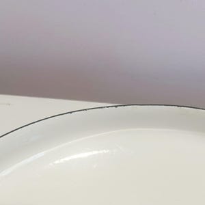 May include: Close-up of the white enamel rim of a round baking dish. The rim has a thin black line around the edge.
