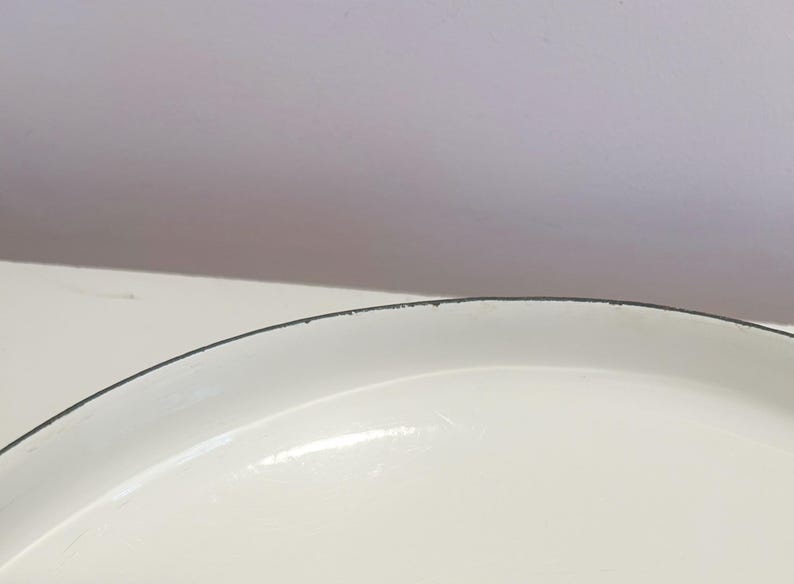May include: Close-up of the white enamel rim of a round baking dish. The rim has a thin black line around the edge.