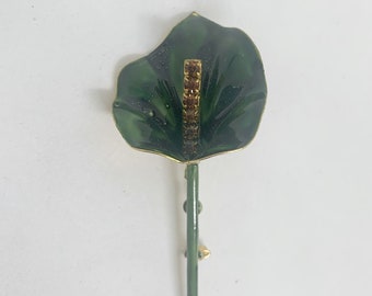 May include: A green enamel flower brooch with a single row of brown rhinestones in the center. The flower has a long stem with a gold pin on the back.