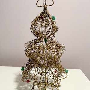 Op de afbeelding: Een gouden draad kerstboom ornament met rode en groene glazen kralen. De boom is gemaakt van gedraaid draad en heeft een stervormige topper.