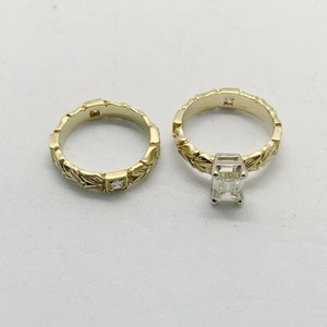 May include: A pair of gold wedding bands with intricate leaf designs. The band on the right has a square-shaped diamond set in the center.