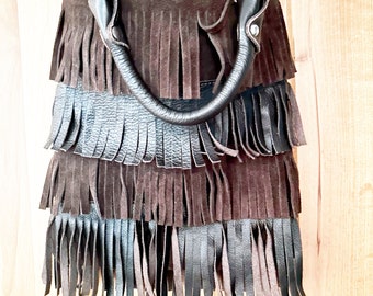May include: A brown leather handbag with fringe detailing. The bag has a top handle and a shoulder strap.