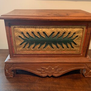 May include: A wooden box with a carved base and a green and gold painted front panel. The box features a decorative design with a carved floral motif.