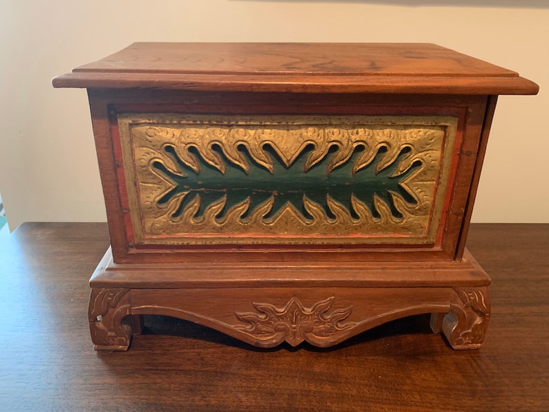 May include: A wooden box with a carved base and a green and gold painted front panel. The box features a decorative design with a carved floral motif.
