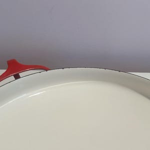 May include: White enamel cast iron pot with a red handle. The pot has a black rim around the top.