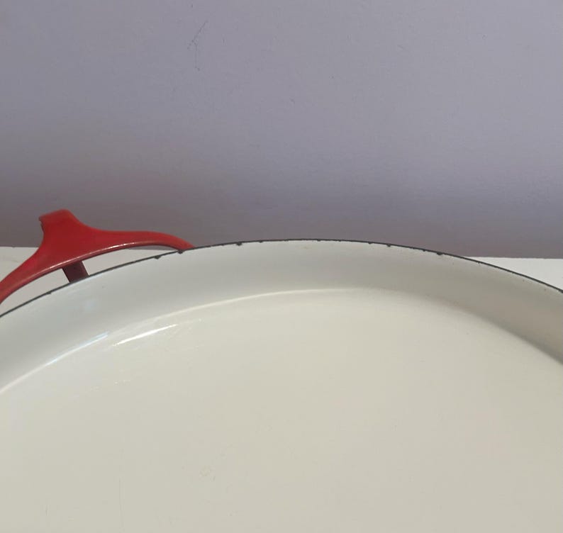 May include: White enamel cast iron pot with a red handle. The pot has a black rim around the top.