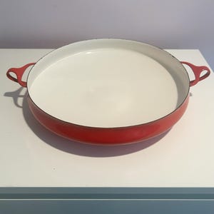 May include: A red enamel cast iron baking dish with white interior and two handles.