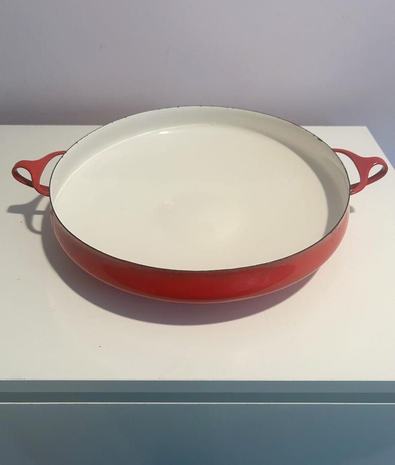 May include: A red enamel cast iron baking dish with white interior and two handles.