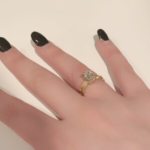 May include: A gold ring with a large, clear, rectangular-shaped diamond. The ring has a textured band.