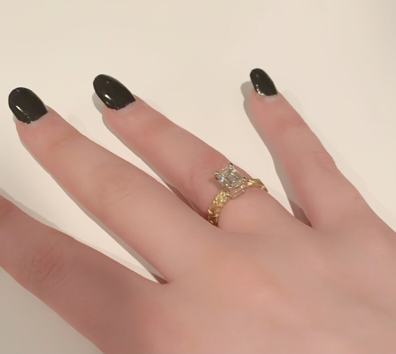 May include: A gold ring with a large, clear, rectangular-shaped diamond. The ring has a textured band.